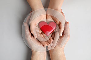 Young and elderly women holding red heart on light grey background, top view