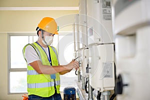 Young electrical engineer wearing a mask Inspect the photovoltaic control panel and indoor electrical control system by a