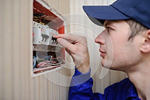 young electrician in blue overall disassembling a electrical panel with fuses in a house