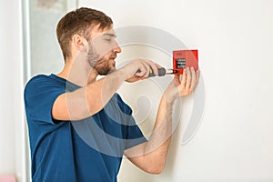 Young electrician installing fire alarm unit on wall
