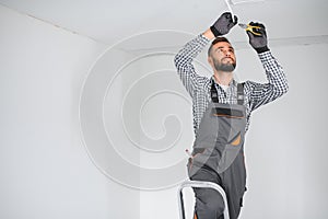 Young electrician installing smoke detector on ceiling.