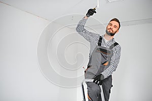 Young electrician installing smoke detector on ceiling.