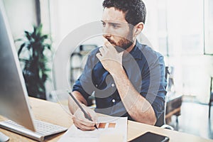 Young elegant banking finance analyst working at sunny office on laptop while sitting at wooden table.Businessman