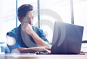 Young elegant banking finance analyst working at sunny office on laptop while sitting at wooden table.Businessman