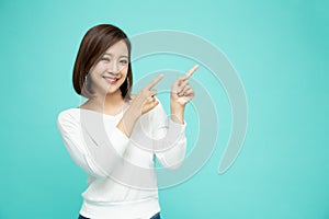 Young elegant beautiful Asian woman smiling and pointing to empty copy space on green background
