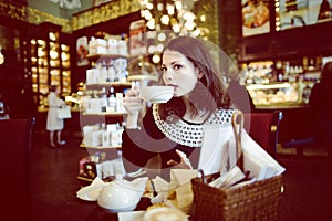 Young elegant brunette woman in cafe drinking coffee, luxury interior