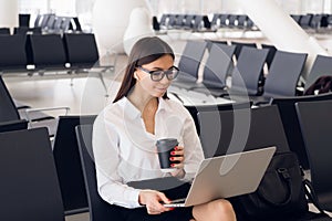 Young elegant business woman in international airport terminal, working on her laptop while waiting for flight