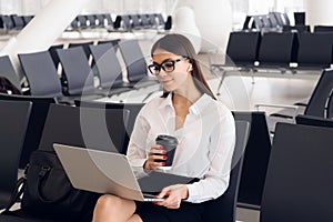 Young elegant business woman in international airport terminal, working on her laptop while waiting for flight