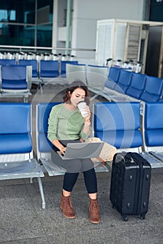 Young elegant business woman in international airport terminal, working on her laptop while waiting for flight