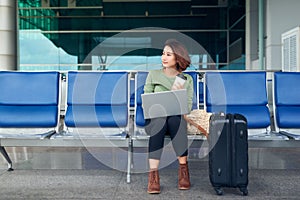 Young elegant business woman in international airport terminal, working on her laptop while waiting for flight