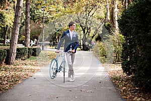 Young elegant businessman with bicycle in the park