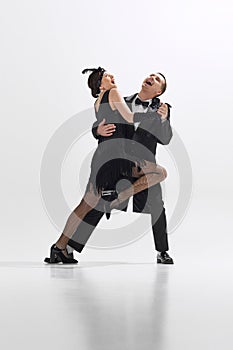 Young elegant couple in vintage black outfits joyously dancing the Roaring Twenties Charleston with expressive emotions photo