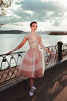 a young elegant female ballerina in a pink dress with a full organza skirt, a ballerina poses near a wrought-iron fence