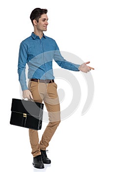 Young elegant man holding suitcase and presenting to side
