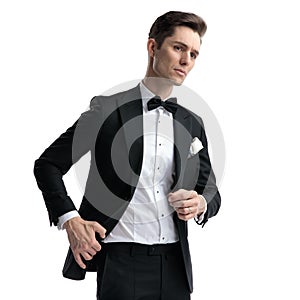 Young elegant man looking to side and pulling coat