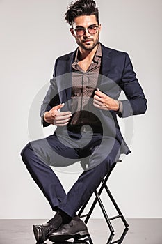 Young elegant man opening his coat sitting on chair