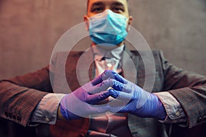 Young elegant man sits in a leather armchair with mask on his face and medical gloves