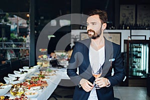 Young elegant man standing in the restaurant, holding a glass of wine. Man's style