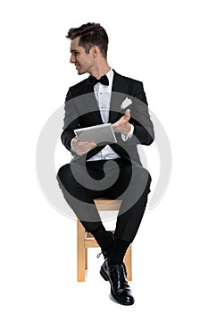 Young elegant man in tuxedo holding tab and looking to side