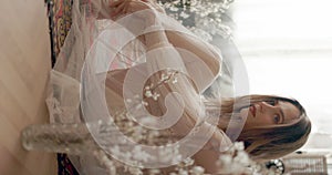 Young elegant model wearing vintage bridal dress sitting on floor, posing at home in stylish vintage interior