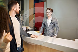 Young elegant salesman talking to a young couple at the dealership showroom.