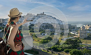 Young elegant tourist taking photos with her smartphone in Ostuni, the white city in the south of italy