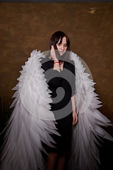 Young elegant woman in trendy black clothes with white wings. Brunette model in nice dark dress posing in studio in