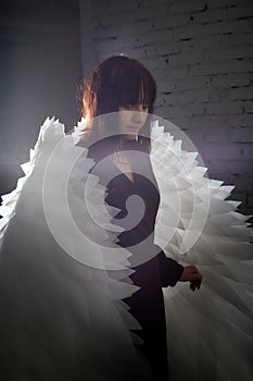 Young elegant woman in trendy black clothes with white wings. Brunette model in nice dark dress posing in studio in