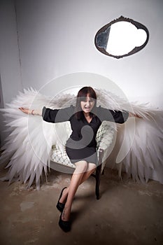 Young elegant woman in trendy black clothes with white wings. Brunette model in nice dark dress posing in studio in