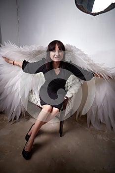 Young elegant woman in trendy black clothes with white wings. Brunette model in nice dark dress posing in studio in