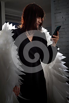 Young elegant woman in trendy black clothes with white wings. Brunette model in nice dress posing in studio in fashion