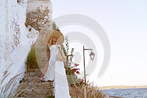 young elegant woman wearing straw hat and white dress standing on stars at old town - Greece, Spetses