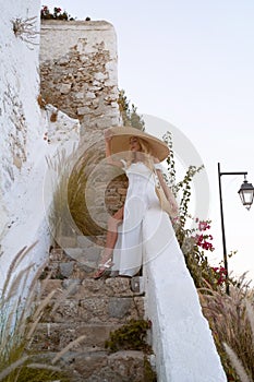 young elegant woman wearing straw hat and white dress standing on stars at old town - Greece, Spetses