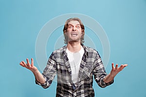 The young emotional angry man screaming on blue studio background