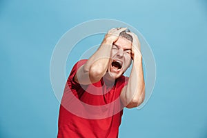 The young emotional angry man screaming on blue studio background