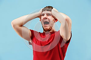 The young emotional angry man screaming on blue studio background