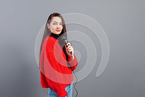 Mladý citový bruneta mikrofon oblečený v svetr zpívá nebo říká řeč 