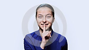 Young emotional female showing sign secret, on light background