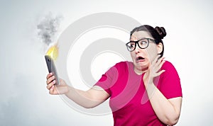 Young emotional girl with fear looks at a smartphone burning in her hands. The situation with fire phone batteries.