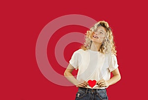 Young emotional girl with a red heart in her hands is standing on an isolated red background. Lovers day concept,Valentine`s Day