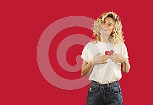 Young emotional girl with a red heart in her hands is standing on an isolated red background. Lovers day concept,Valentine`s Day