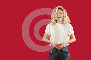 Young emotional girl with a red heart in her hands is standing on an isolated red background. Lovers day concept,Valentine`s Day