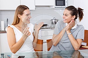 Young emotional girlfriends chatting and looking betrothal ring at home