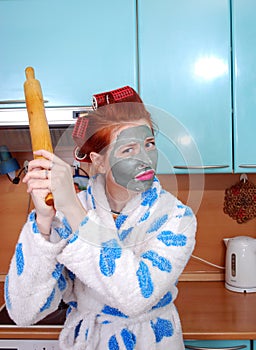 The young emotional housewife with red hair, in hair curlers, and with a clay mask on a face dissatisfied, threatens having threat