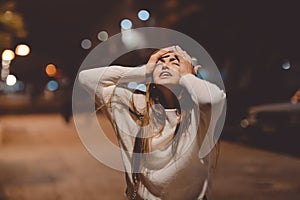 Young emotional stressed woman screaming looking up, city street in the night, evening lights bokeh background outdoors