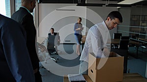 Young employee unpack box with docs and equipment. His colleagues walking near in modern office