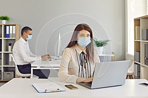 Young employees in medical face masks working on computers in the company office