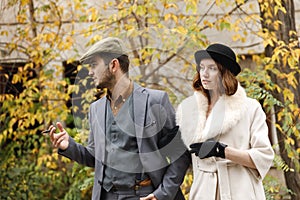 A young gangster retro couple walking holding hands. The guy is smoking a cigar, and girl is watching to him. Retro.