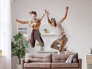 Young energetic active african american family couple jumping on sofa, having fun together at home