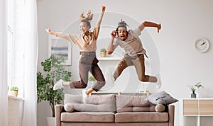 Young energetic active african american family couple jumping on sofa, having fun together at home